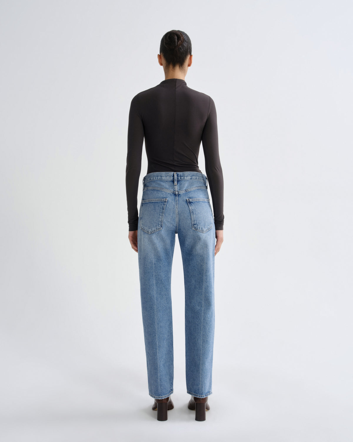 Person wearing blue jeans and a black top on a white background