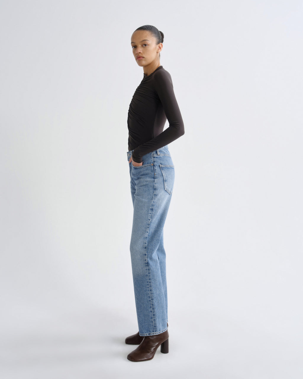 Person wearing a black long-sleeve top and light blue jeans on a white background
