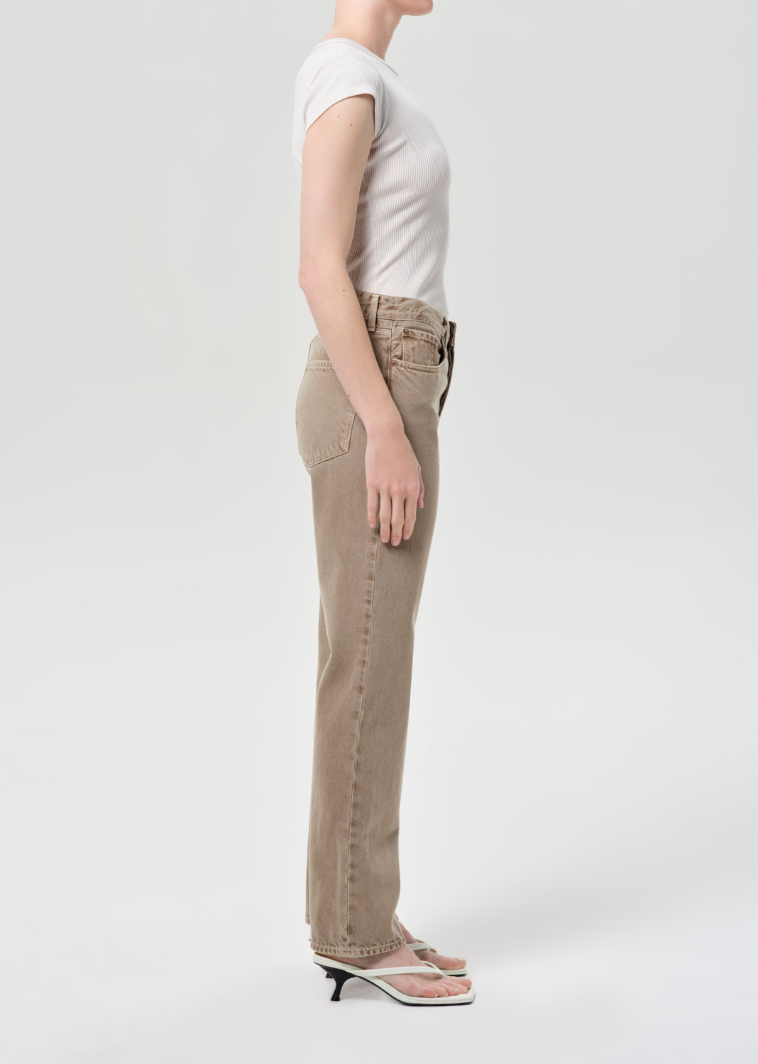 Person wearing beige pants and a white top on a light gray background