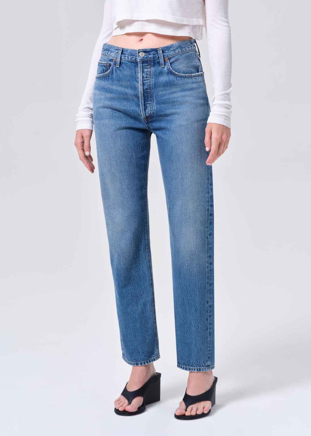 Person wearing blue jeans and a white top on a plain background