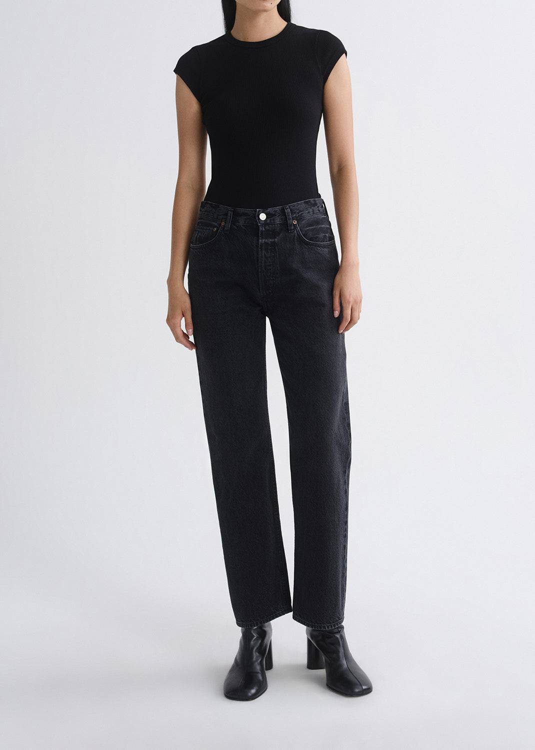 Person wearing black cap-sleeve top and black jeans on a grey background
