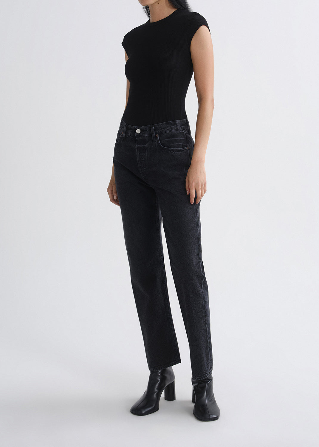 Person wearing a black sleeveless top and black jeans on a grey background