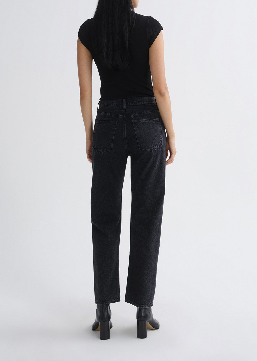 Person wearing black cap-sleeve top and black jeans on a grey background