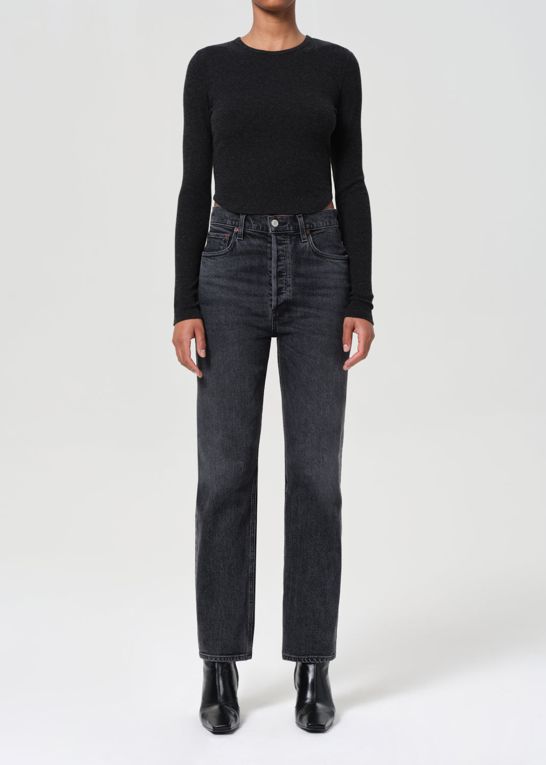 Person wearing a black long-sleeve top and dark gray jeans on a white background