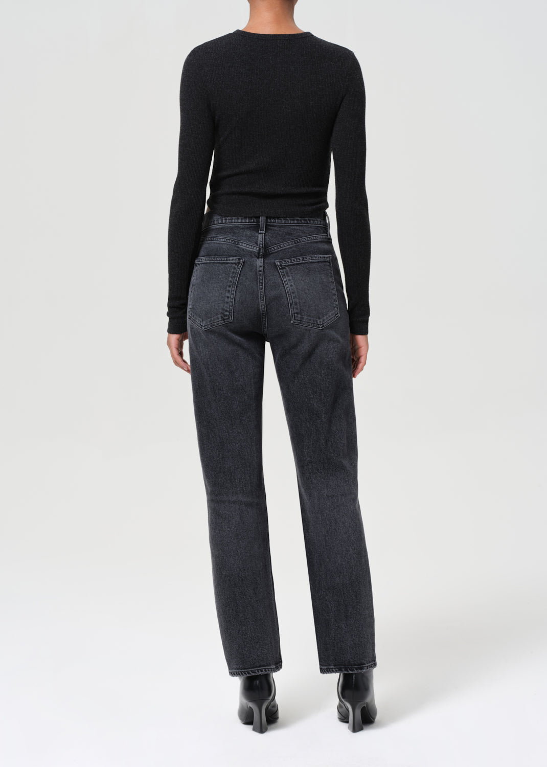 Person wearing black long-sleeve top and dark gray jeans on a white background
