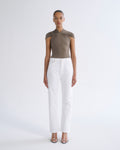 A model stands against a light gray studio background wearing a taupe-brown draped short-sleeve top and white straight-leg jeans with clear-strap heeled sandals.