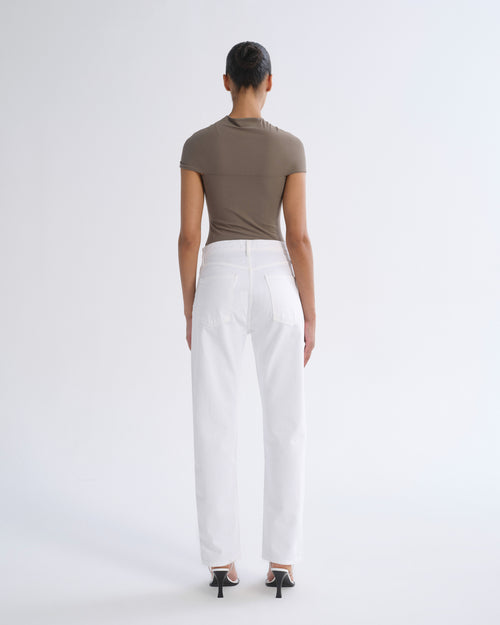 A model shown from the back wearing a fitted taupe short-sleeve top and white wide-leg trousers, paired with black high-heeled sandals, against a plain light gray studio background.