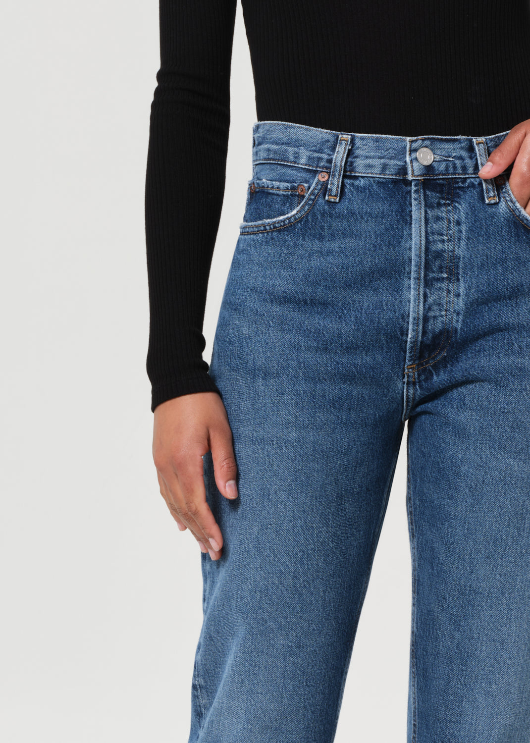 Person wearing blue jeans and a black long-sleeve top on a light gray background