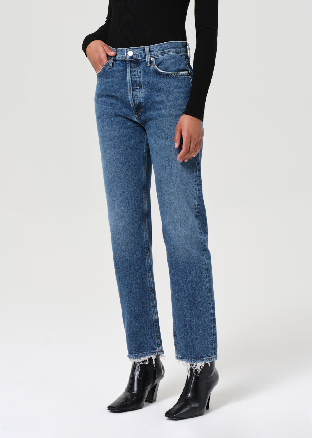 Person wearing blue jeans and black boots on a white background