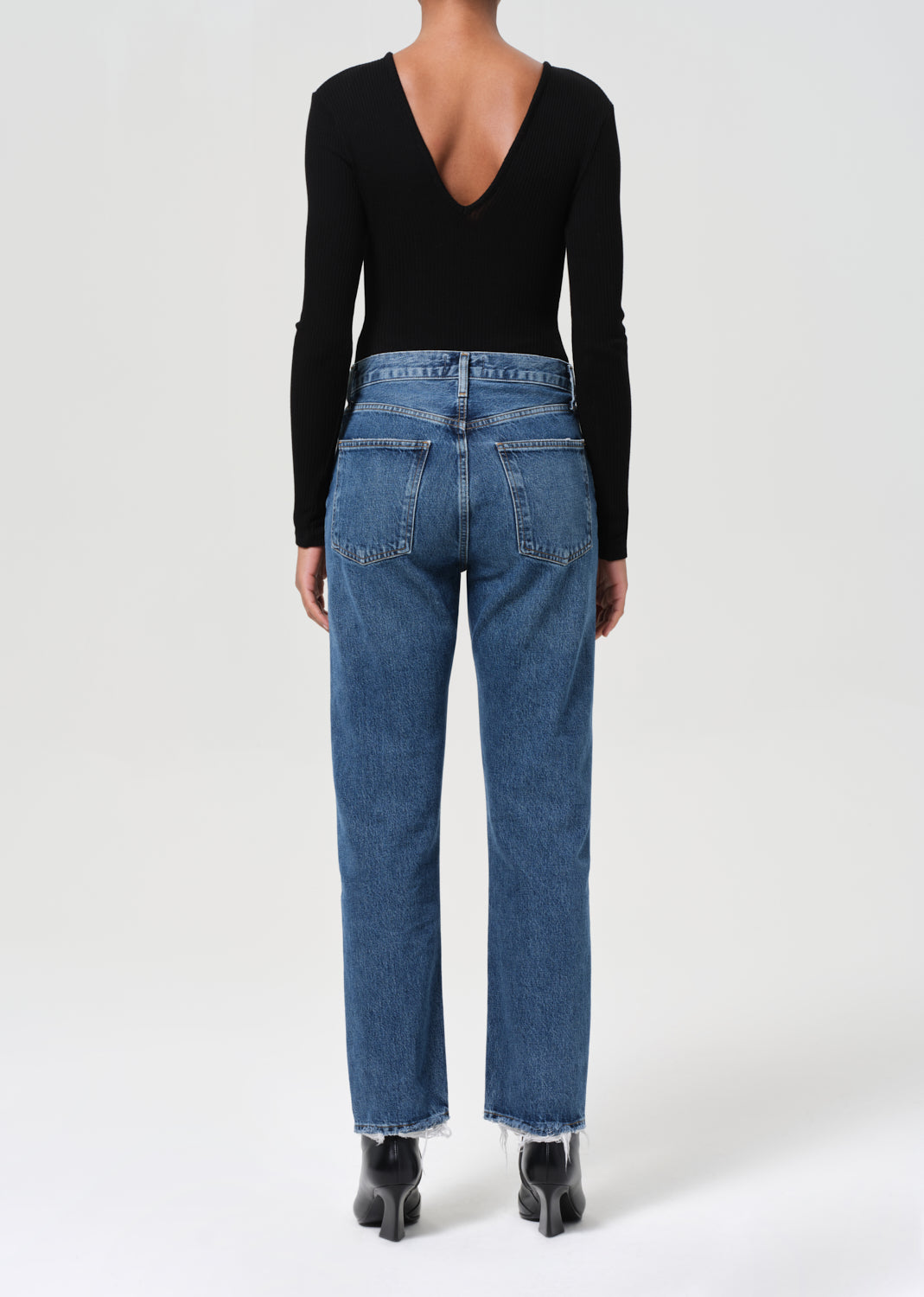 Person wearing blue jeans and a black long-sleeve top on a white background
