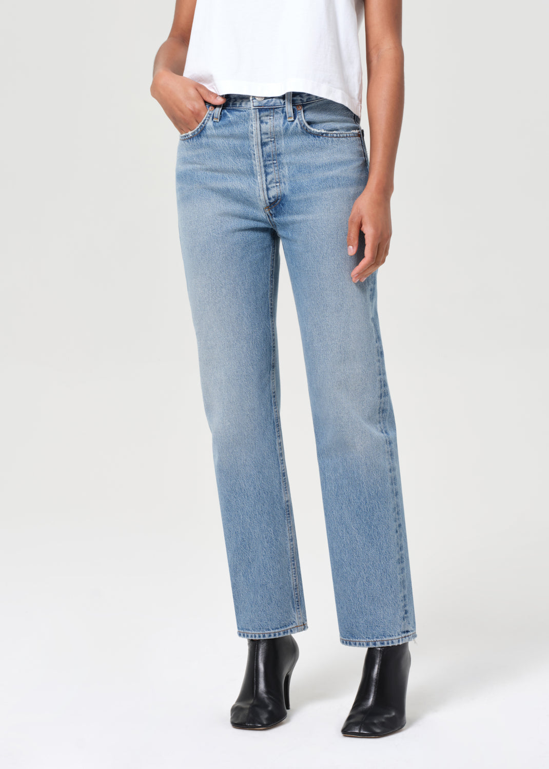 Person wearing light blue jeans and black boots on a white background