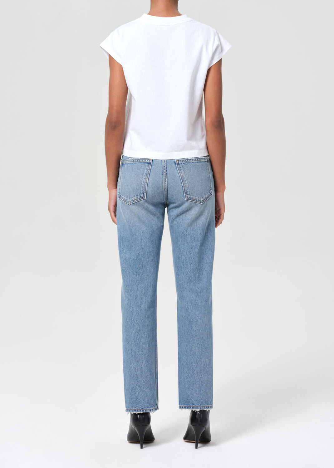 Person wearing light blue jeans and a white top on a plain background