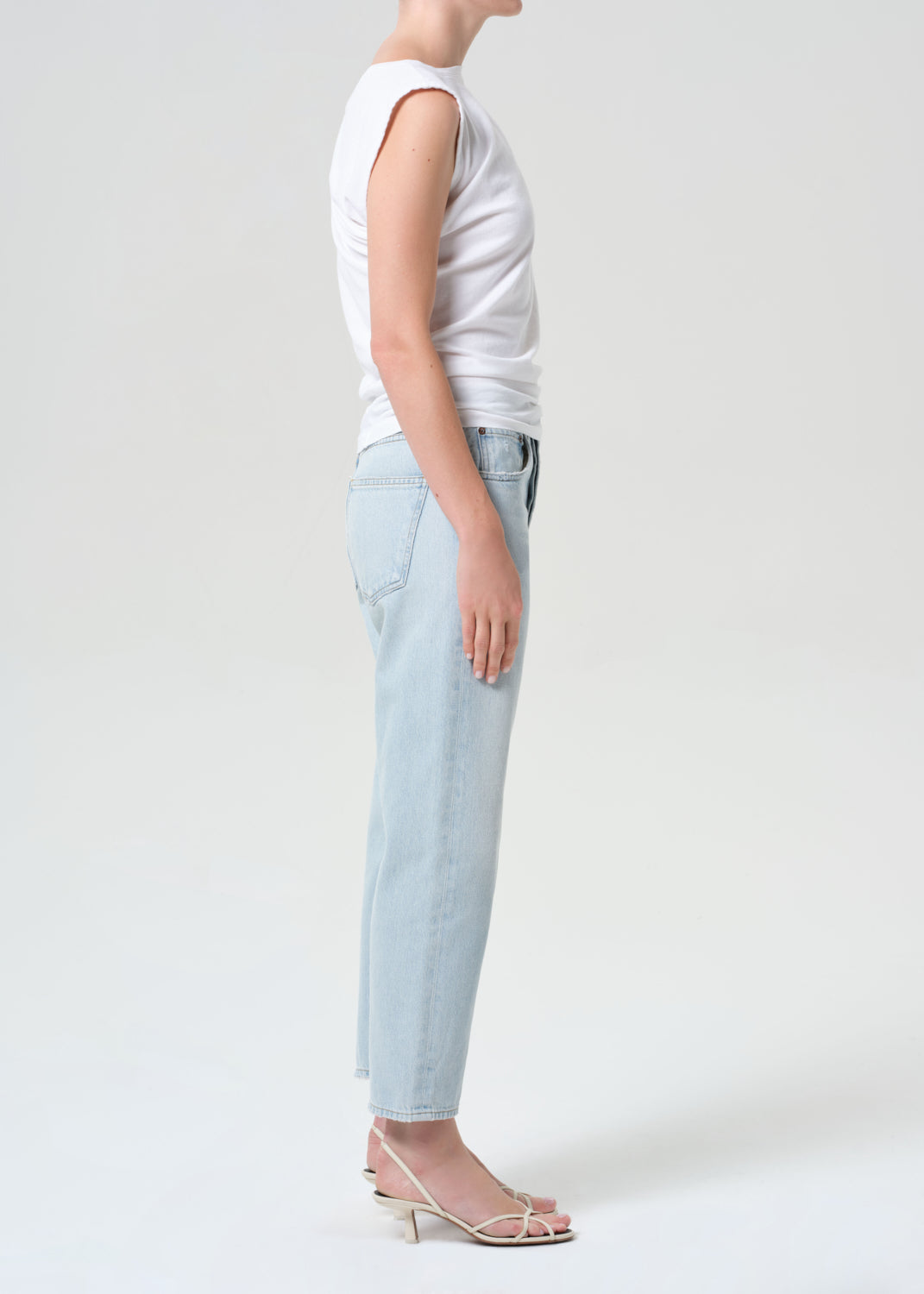 Person wearing a white sleeveless top and light blue jeans on a plain background