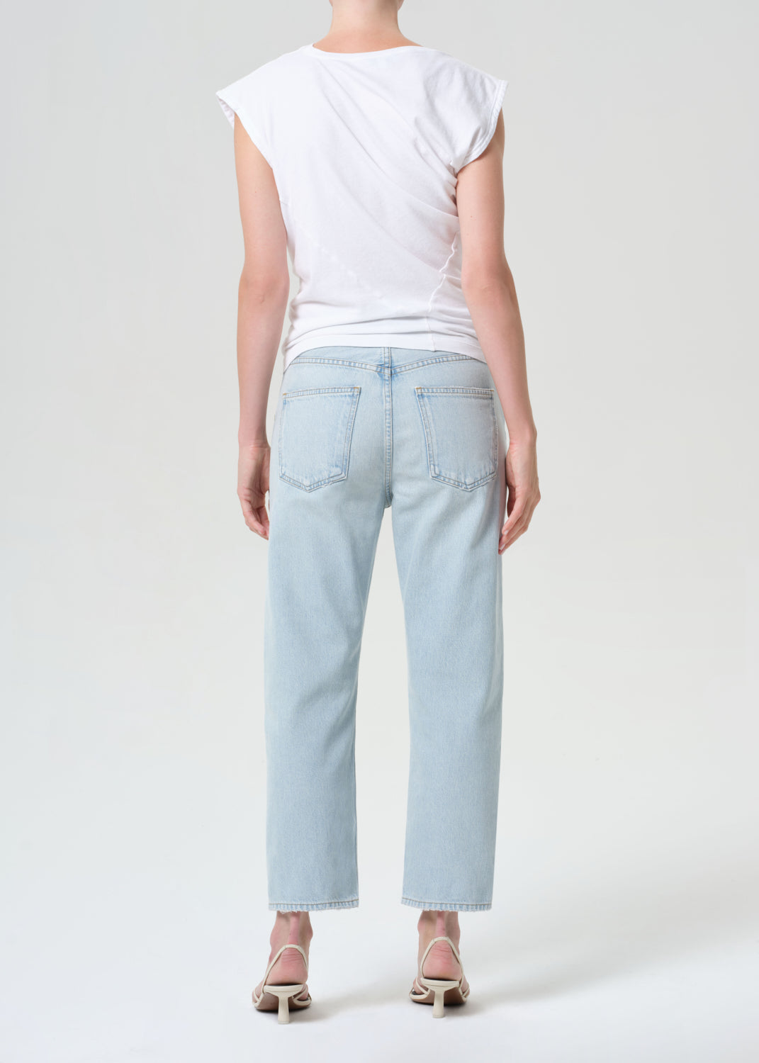 Person wearing light blue jeans and a white top on a plain background