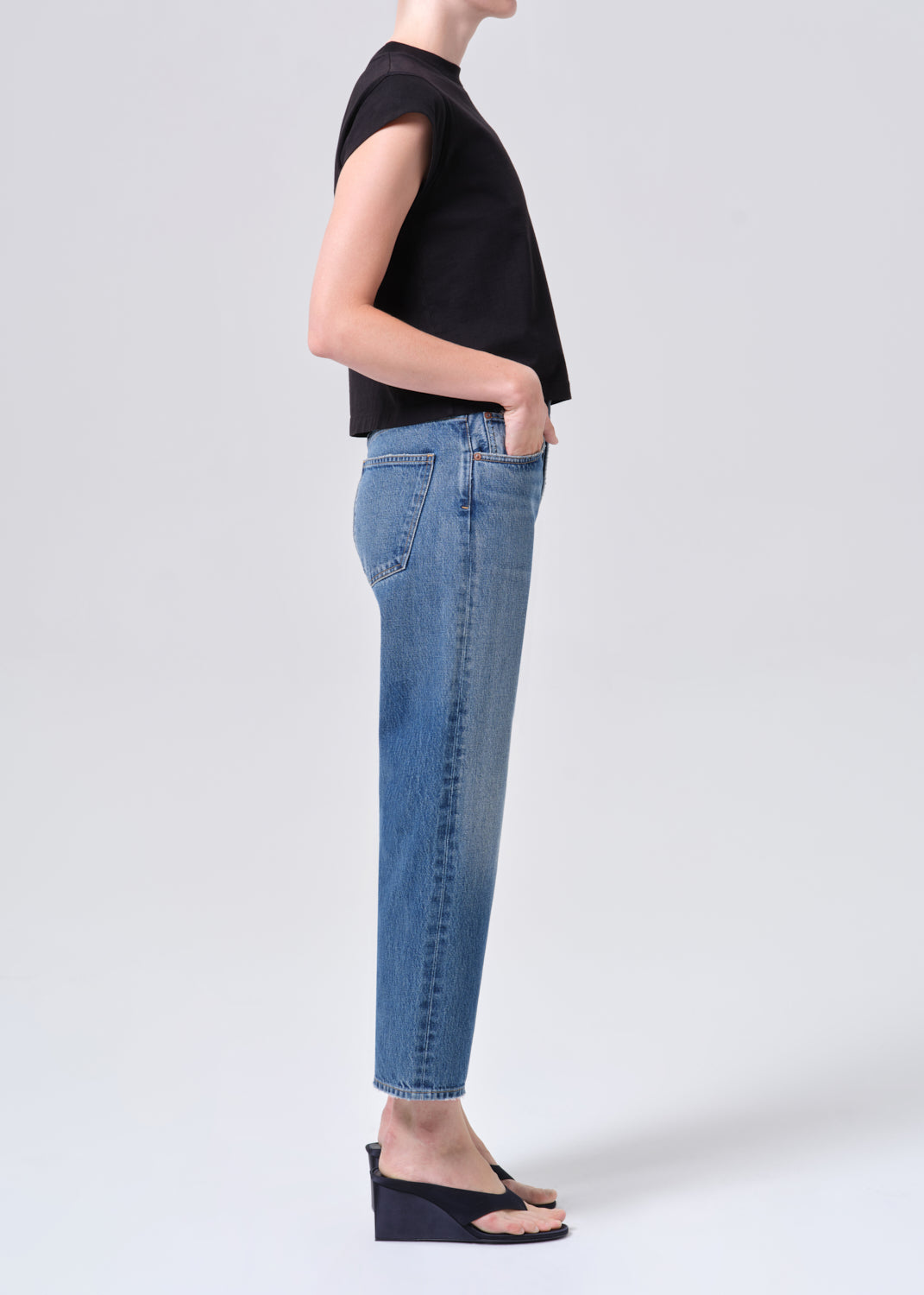 Person wearing a black top and blue jeans on a white background