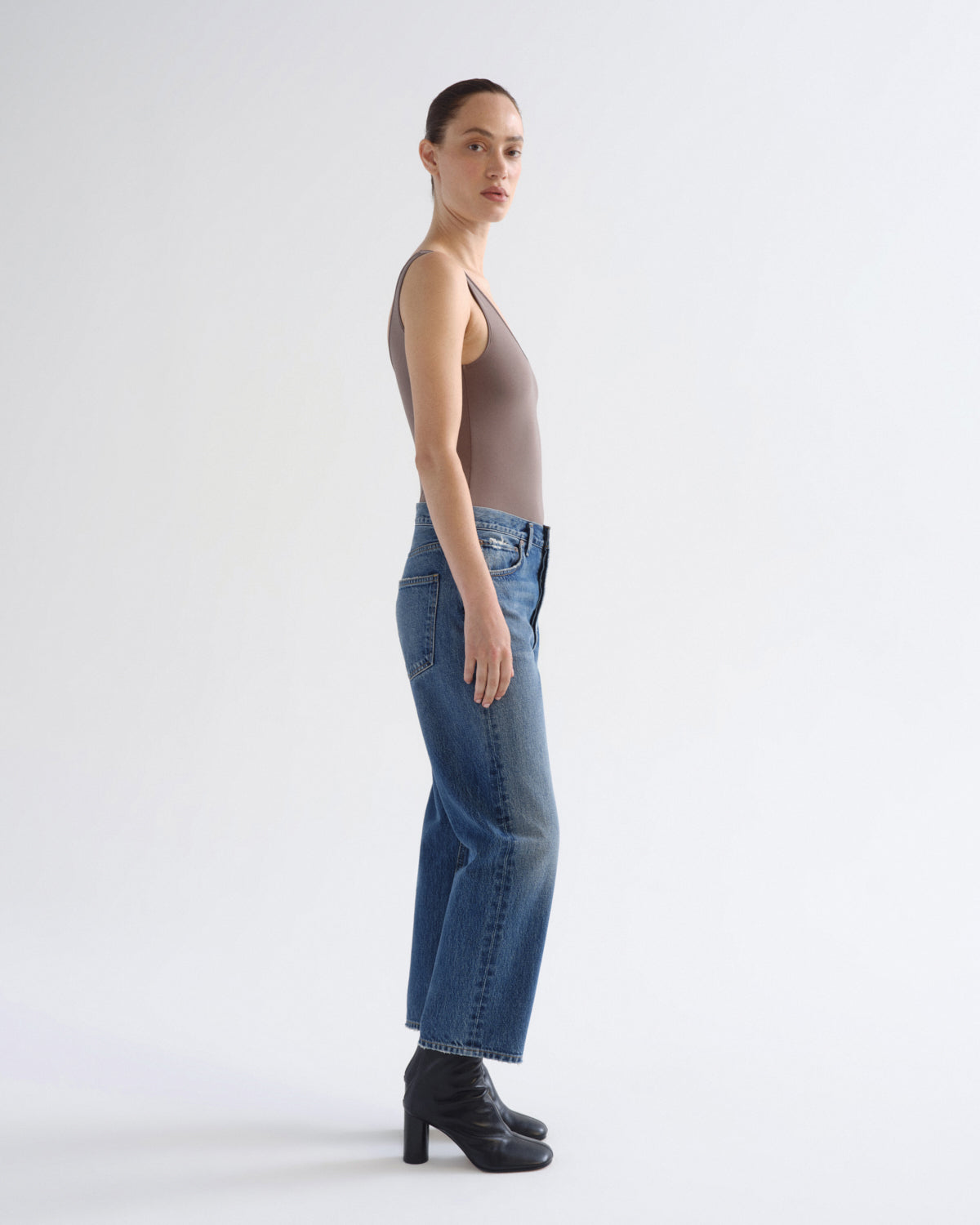 A model shown in profile wearing blue wide-leg cropped jeans, a taupe-brown sleeveless top, and black ankle boots against a plain white studio background.