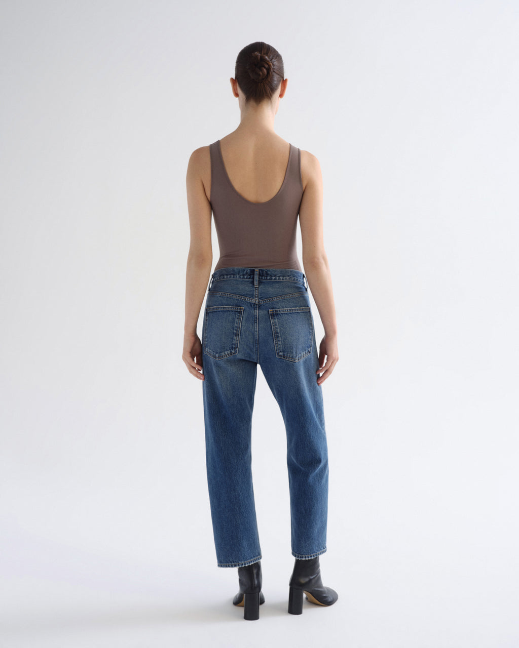 A model shown from the back wearing a brown sleeveless top, blue jeans, and black ankle boots against a plain white studio background.