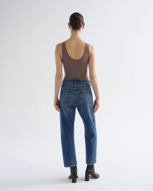A model shown from the back wearing a brown sleeveless top, blue jeans, and black ankle boots against a plain white studio background.
