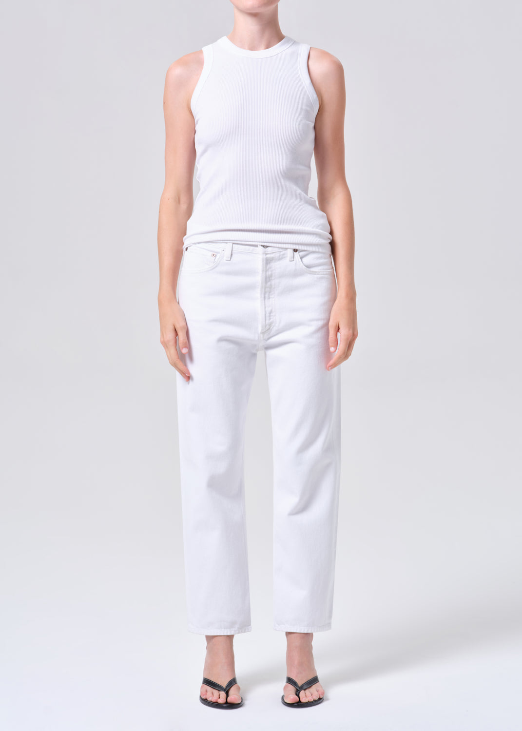 Person wearing a white sleeveless top and white jeans on a light gray background