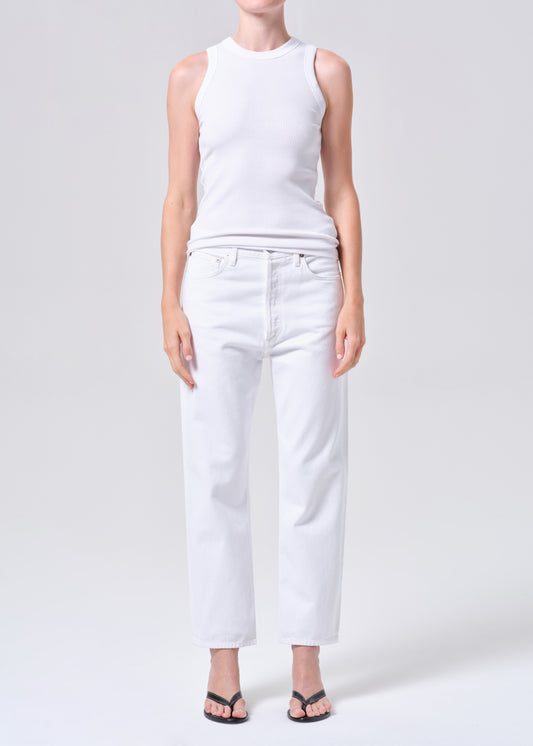 Person wearing a white sleeveless top and white jeans on a light gray background