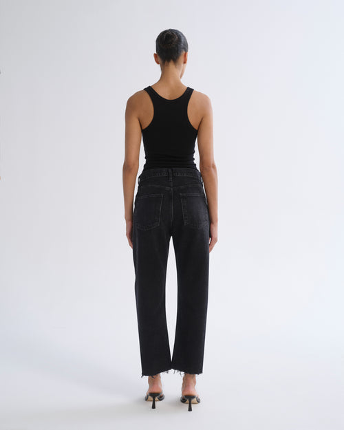 A model viewed from the back wearing a black ribbed tank top and black wide-leg cropped jeans with frayed hems, paired with black high-heeled sandals, against a plain white studio background.