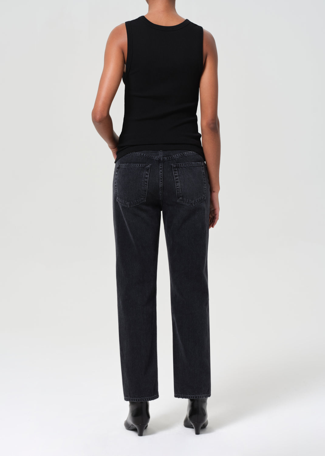 Person wearing a black sleeveless top and black pants on a white background