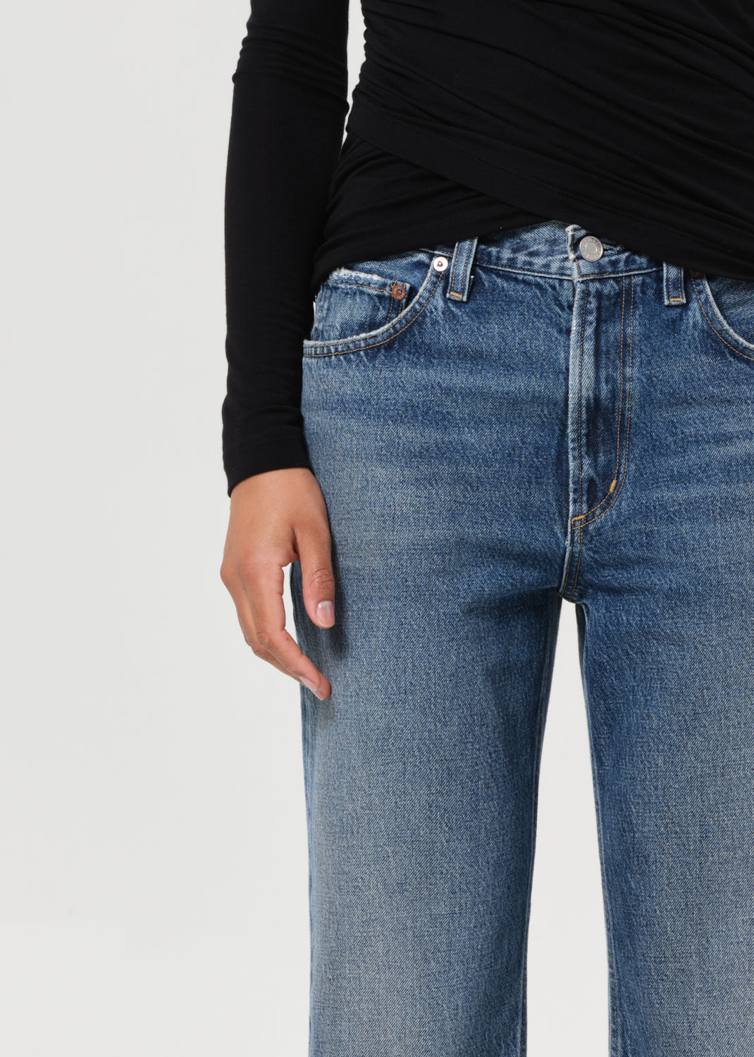 Person wearing blue jeans and a black top on a light gray background