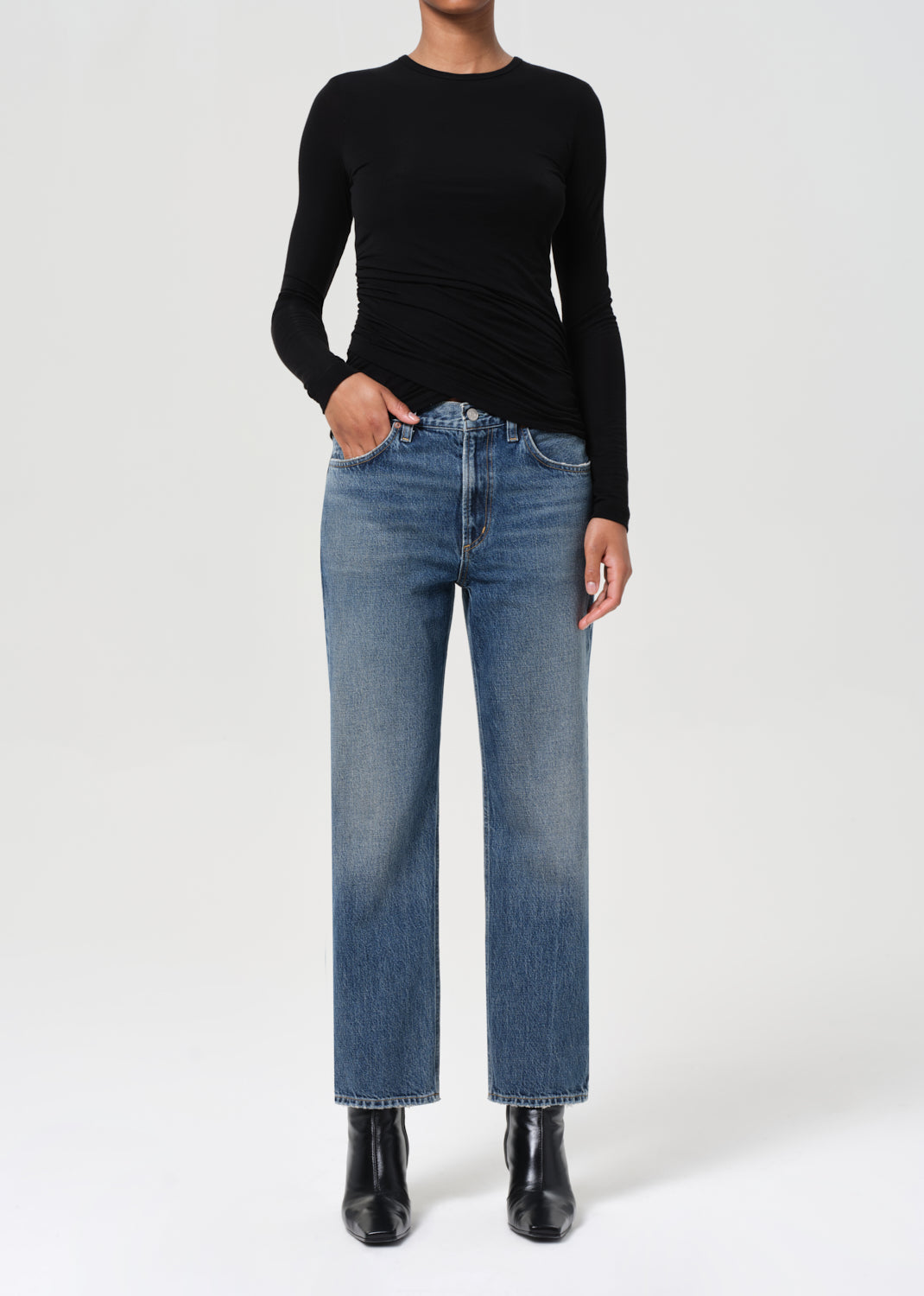 Person wearing a black long-sleeve top and blue jeans on a white background