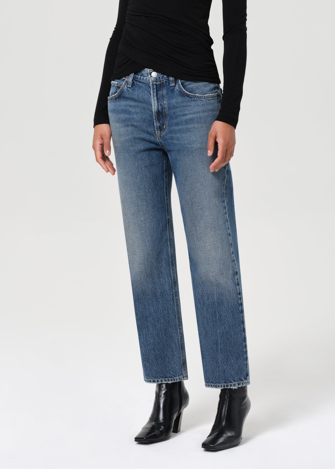 Person wearing blue jeans and black boots on a white background
