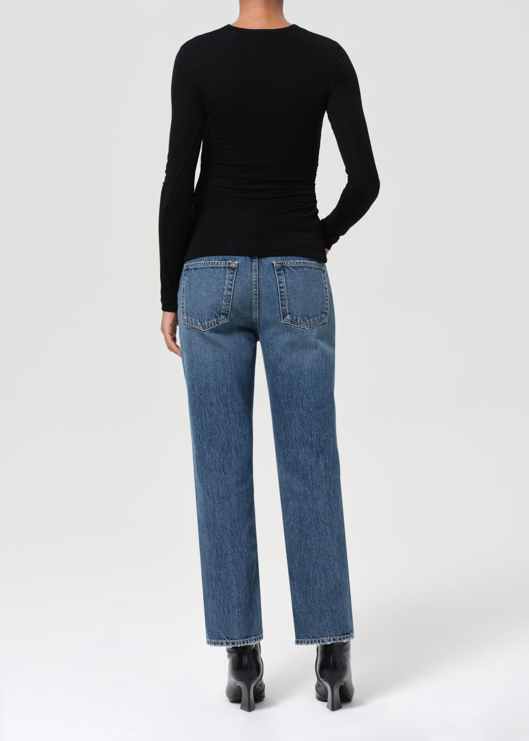 Person wearing blue jeans and a black long-sleeve top on a white background
