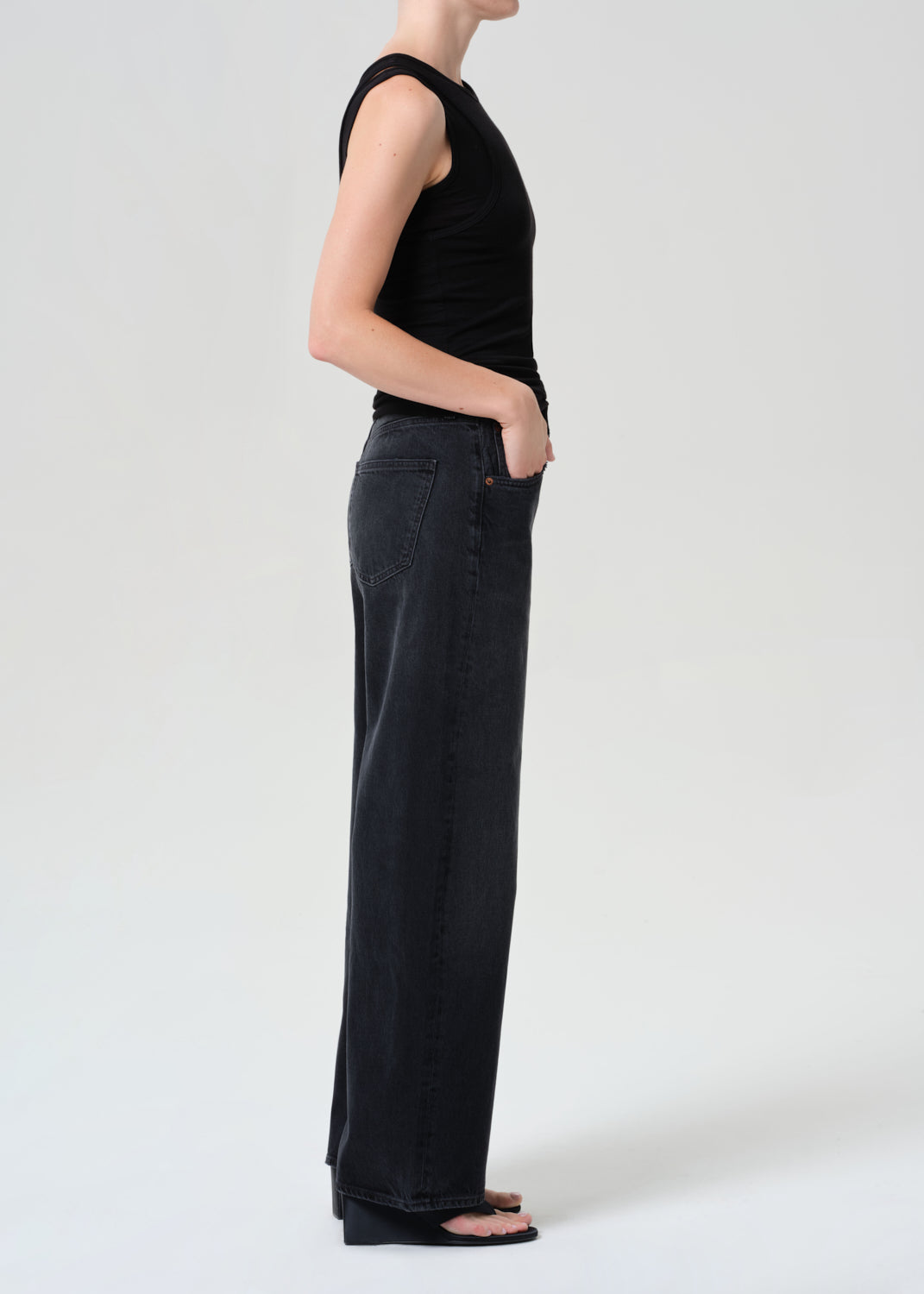 Person wearing black sleeveless top and wide-leg jeans on a white background