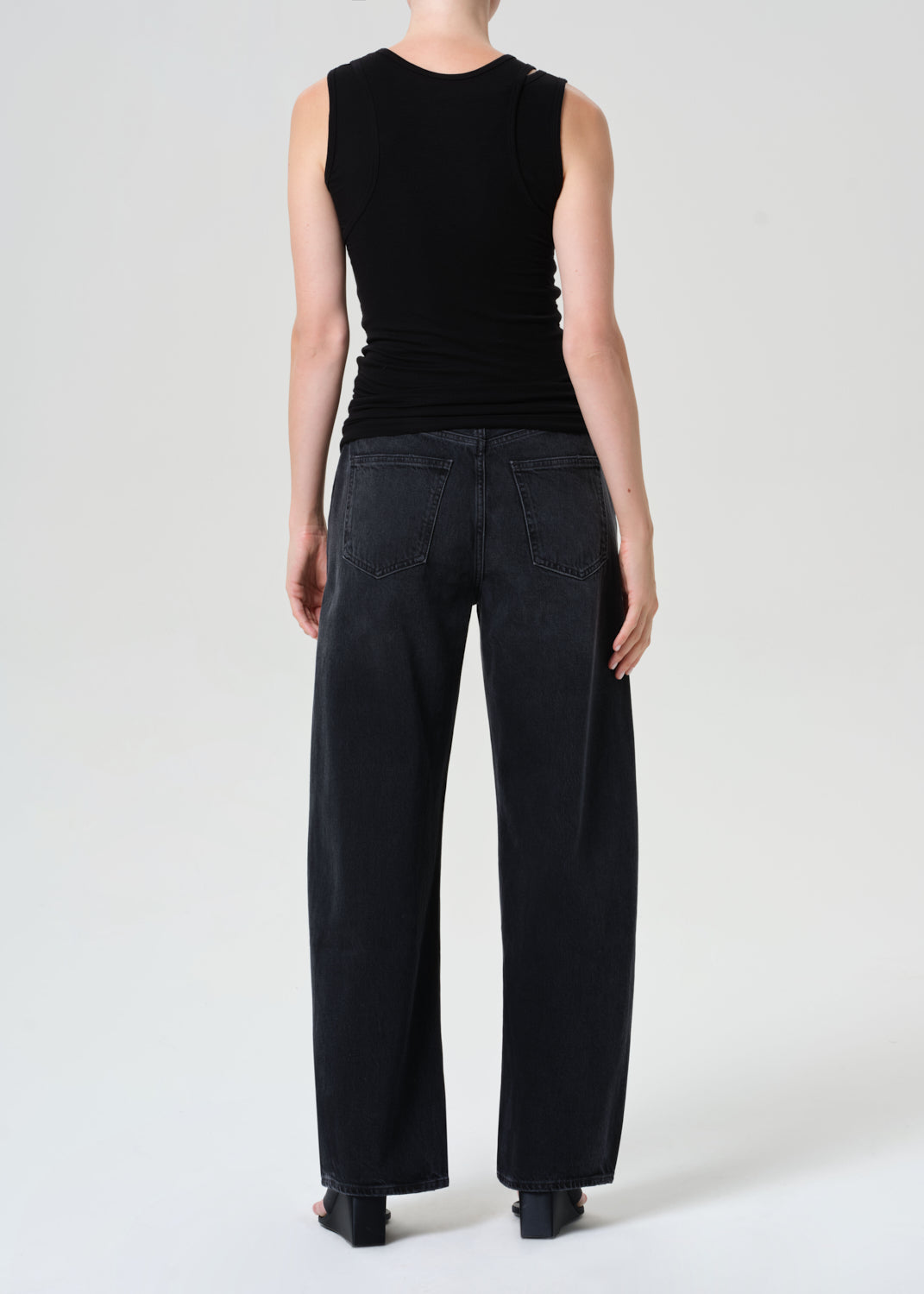 Person wearing a black sleeveless top and black wide-leg pants on a white background