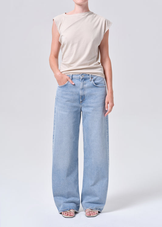 Person wearing a beige sleeveless top and light blue jeans on a white background