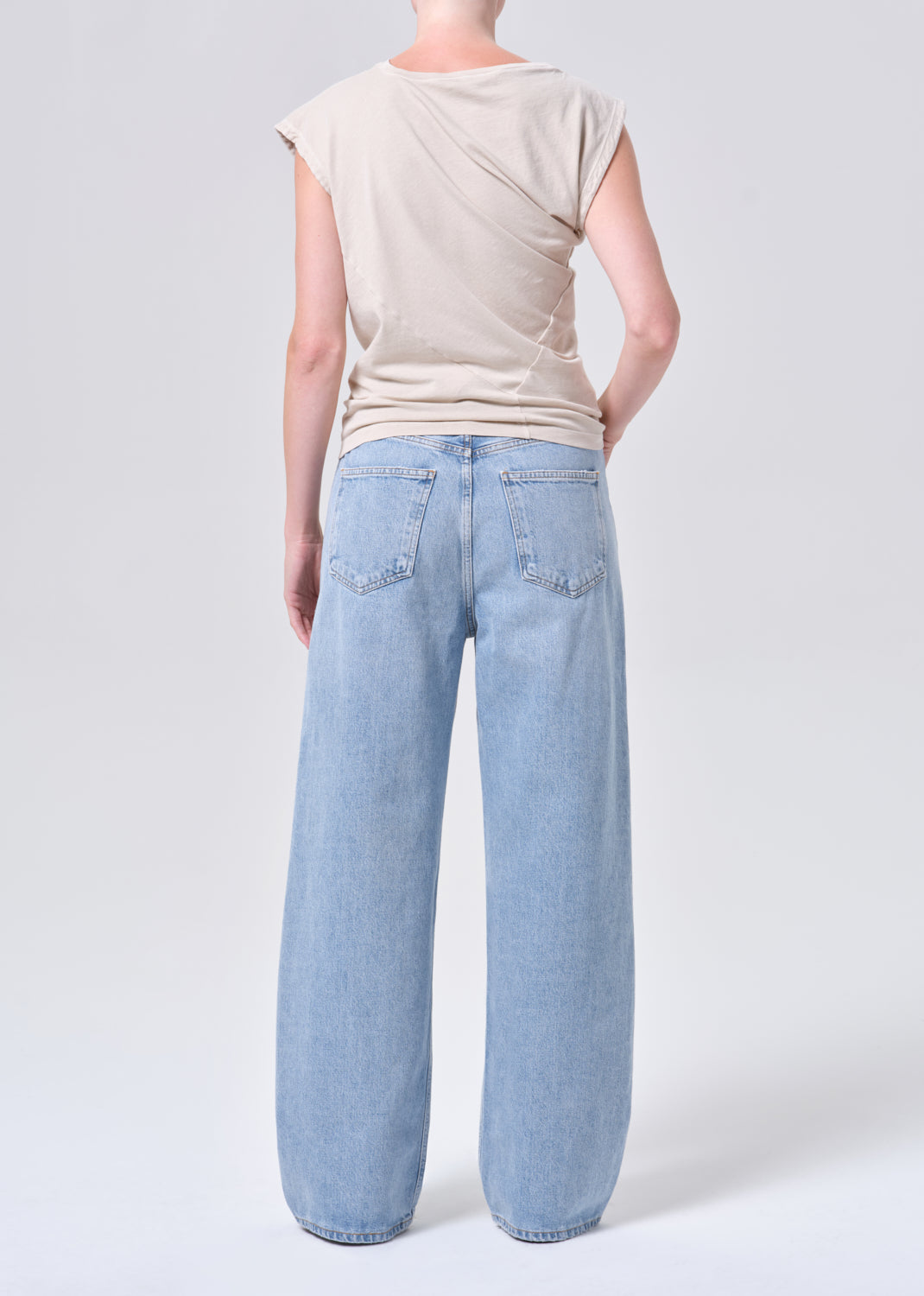 Person wearing light blue jeans and a beige top on a white background