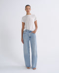 A model stands against a light gray studio background wearing a white short-sleeve t-shirt and light-wash wide-leg blue jeans.