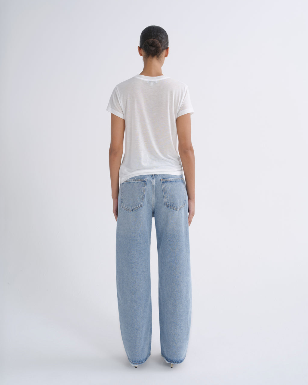 A model viewed from behind wearing a white short-sleeve t-shirt and light-wash wide-leg denim jeans against a plain white studio background.