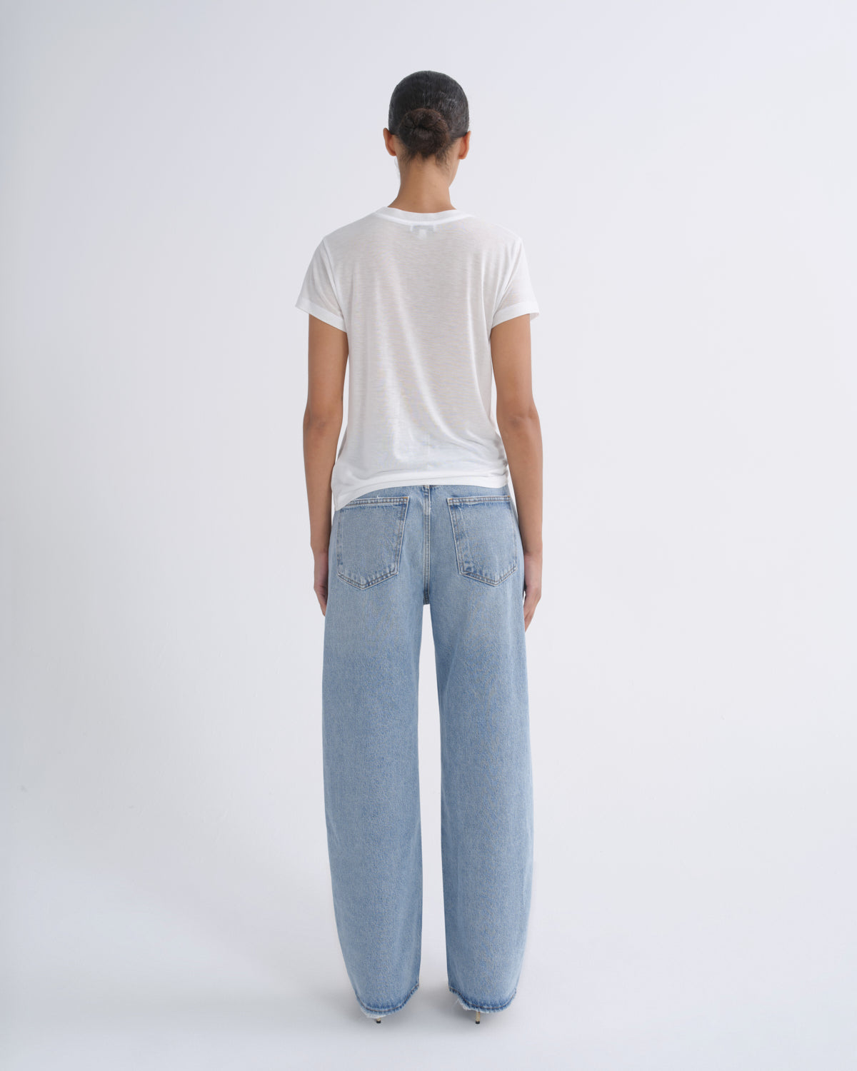 A model viewed from behind wearing a white short-sleeve t-shirt and light-wash wide-leg denim jeans against a plain white studio background.