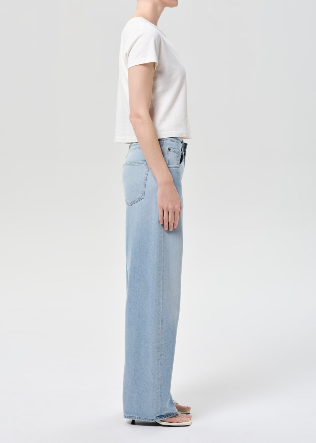 Person wearing light blue jeans and a white t-shirt on a plain background