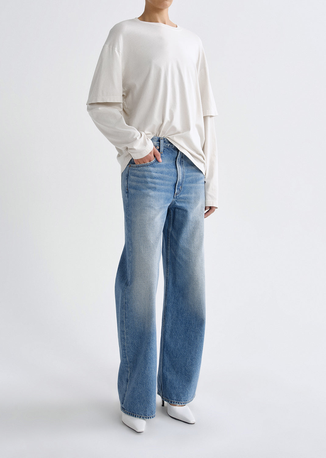 Person wearing a white long sleeve tee with light wash straight leg jeans viewed from the side on a grey background