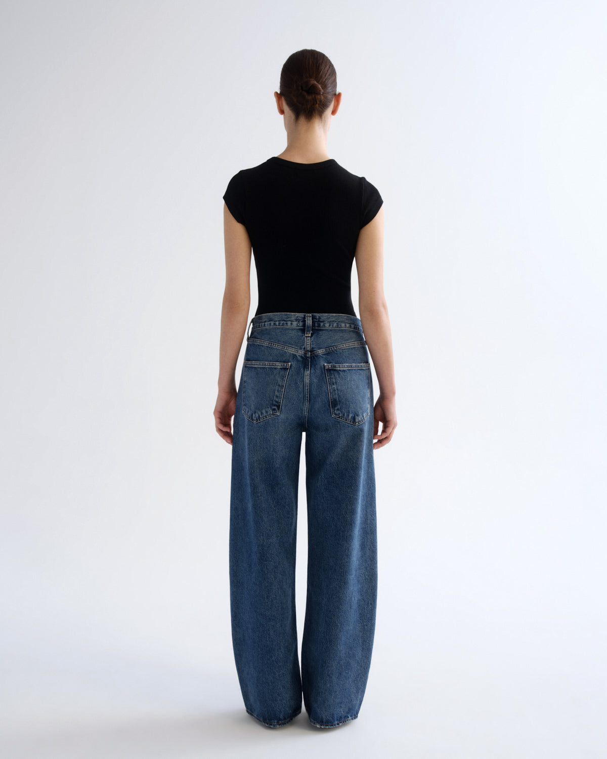 A model shown from the back wearing a black short-sleeve top and wide-leg blue denim jeans against a plain white studio background.