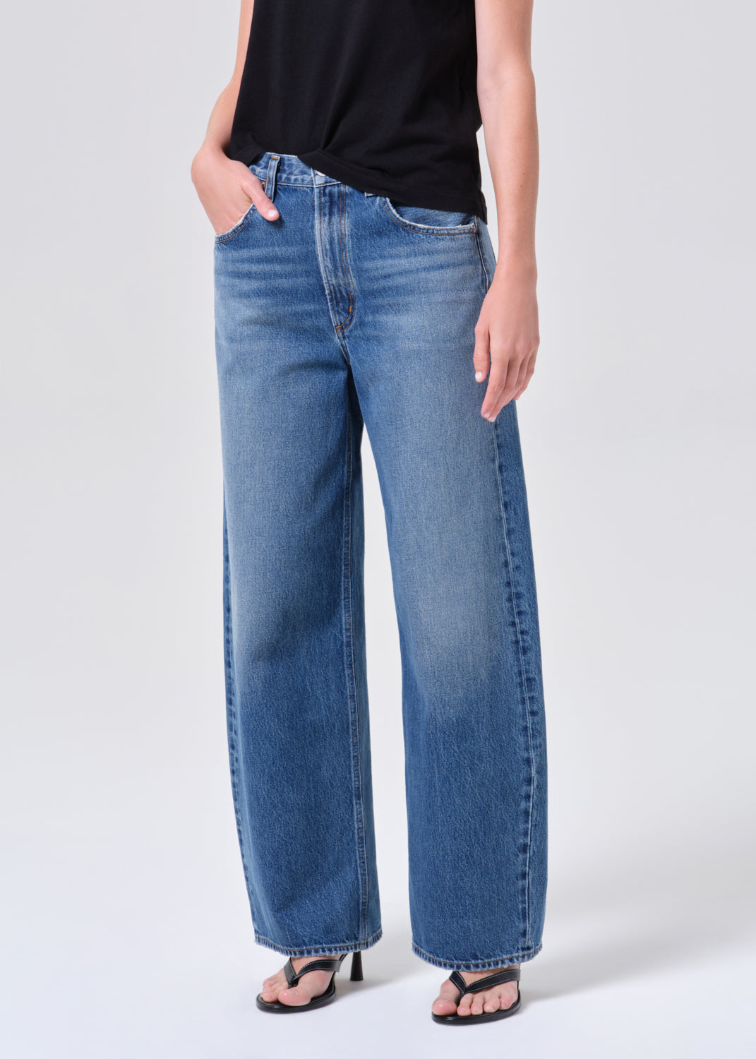 Person wearing blue jeans and a black top on a white background