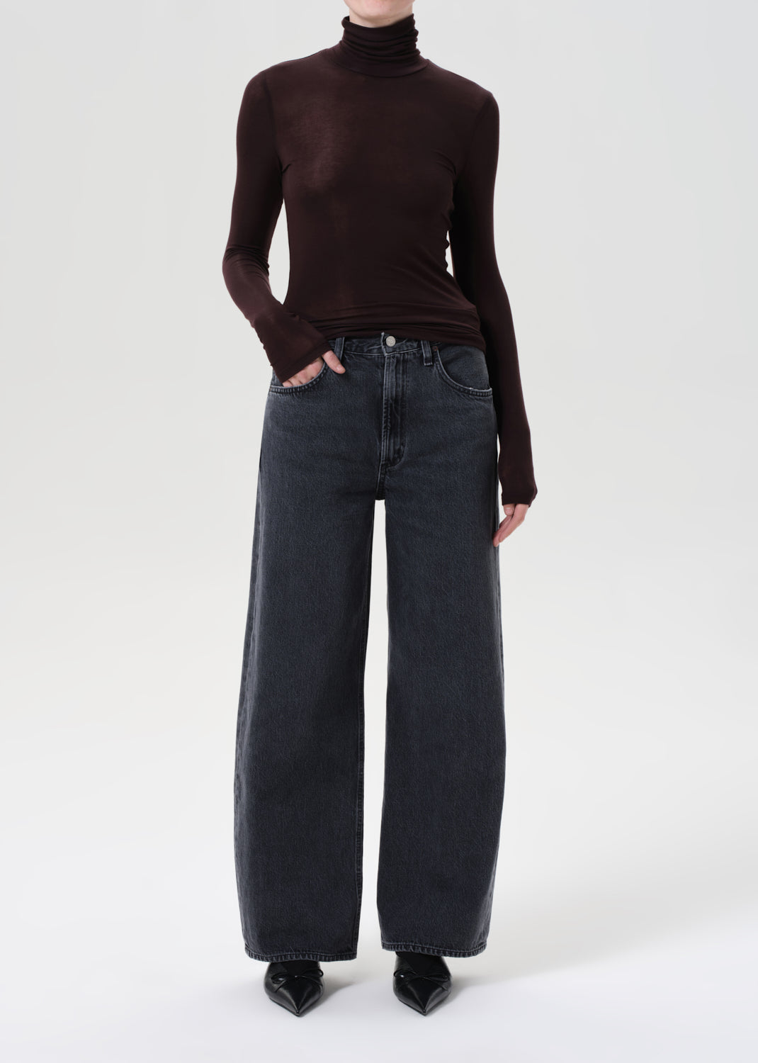 Person wearing a brown turtleneck and dark jeans on a white background