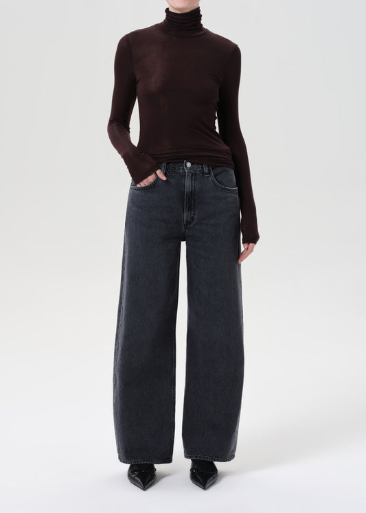 Person wearing a brown turtleneck and dark jeans on a white background