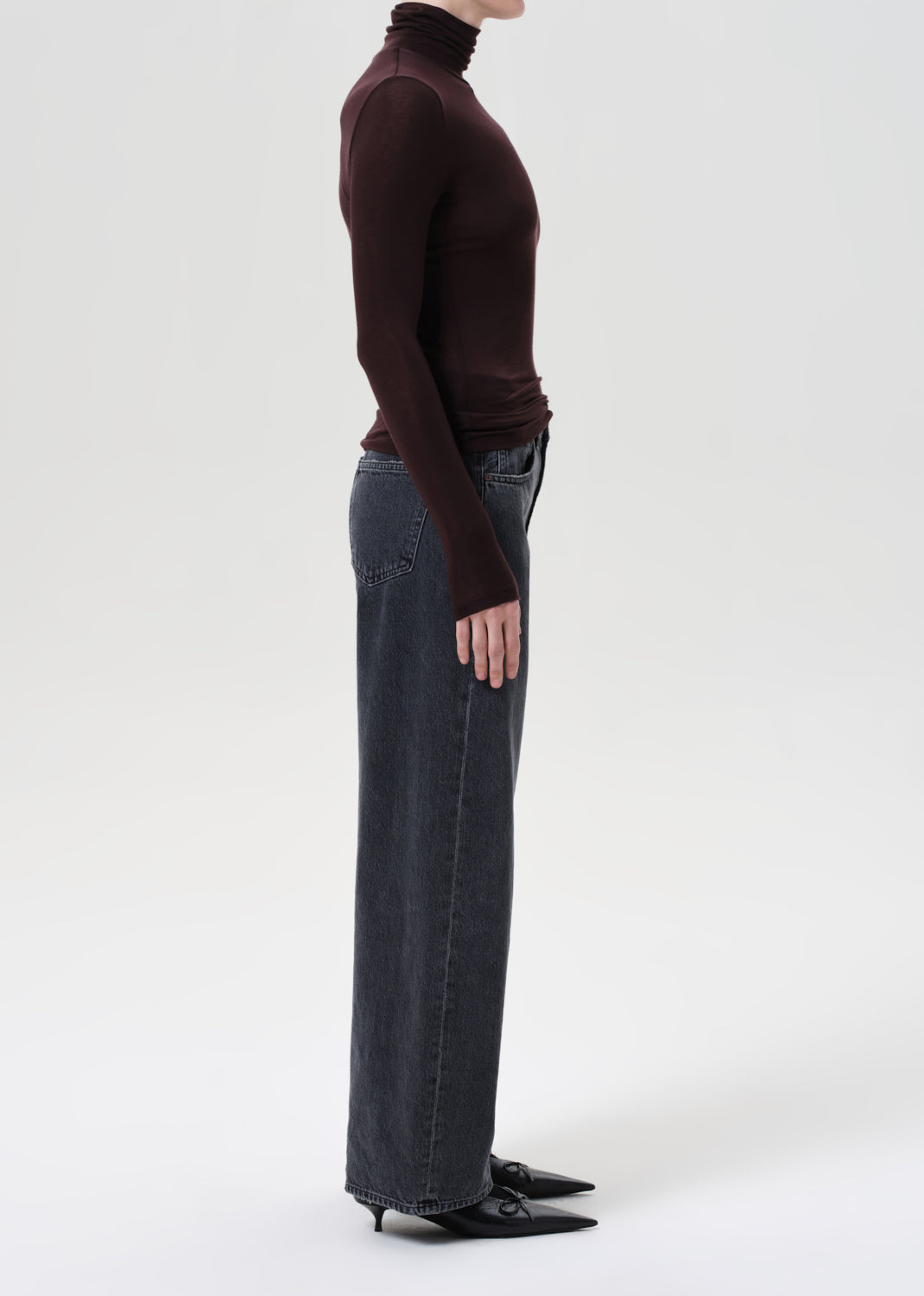 Person wearing a brown turtleneck and blue jeans on a white background