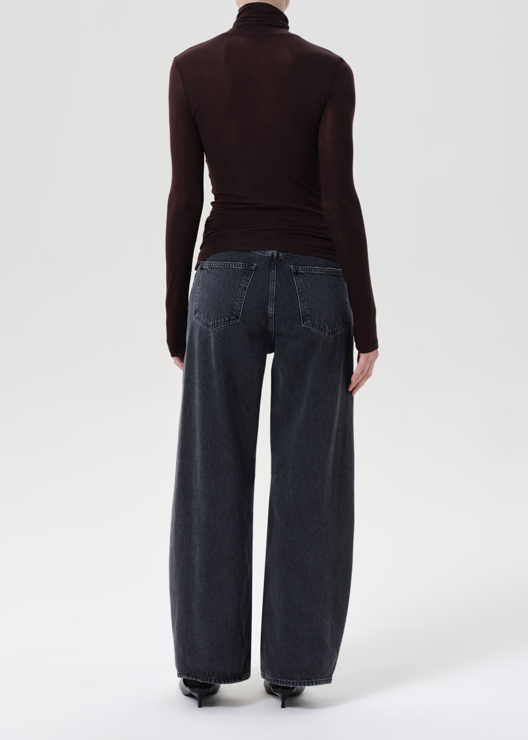 Person wearing a brown turtleneck and dark jeans on a white background