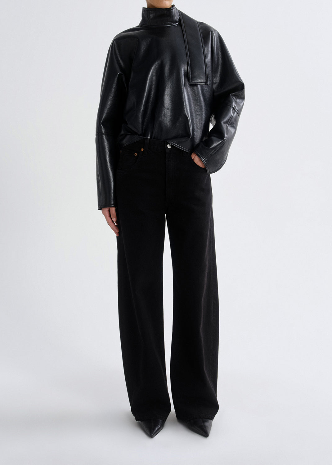 Person wearing a black shiny top and black pants on a grey background