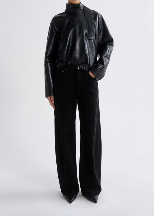 Person wearing a black shiny top and black pants on a grey background