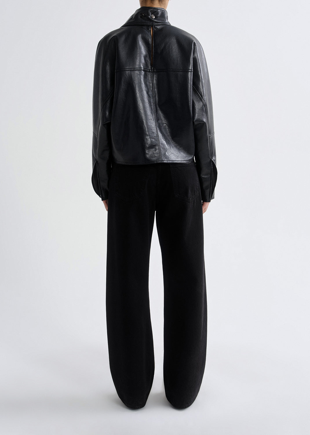 Person wearing a black leather jacket and pants on a grey background