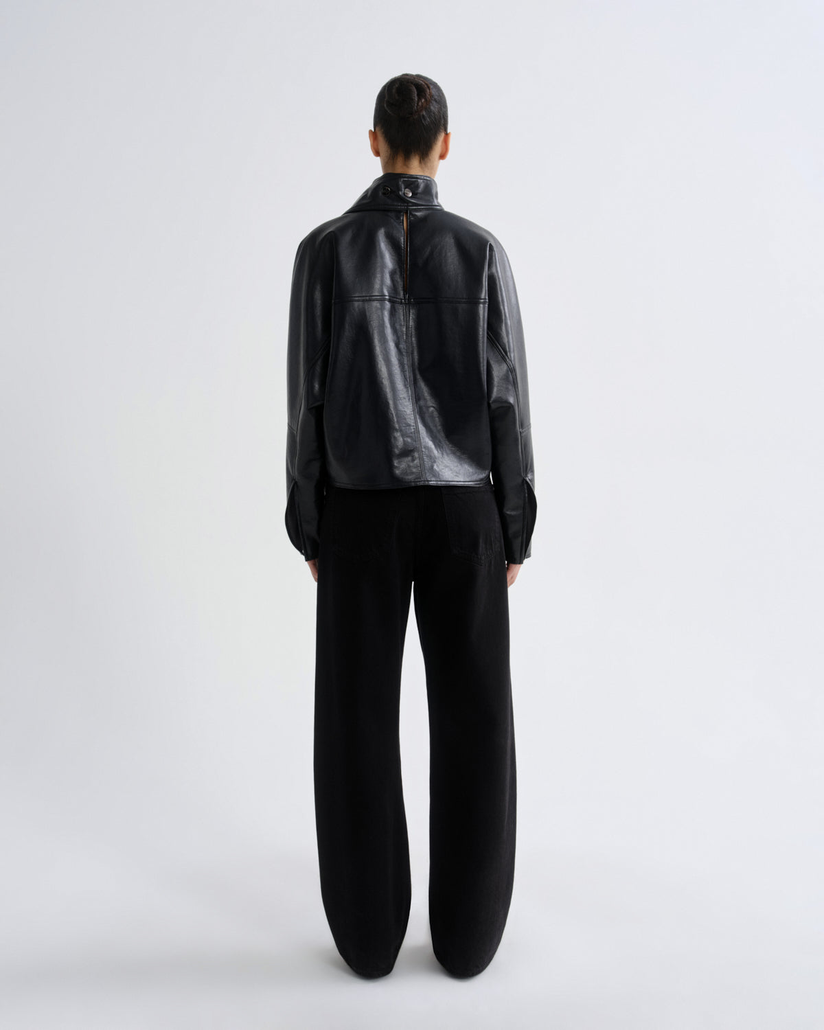 Person wearing a black leather jacket and pants on a white background