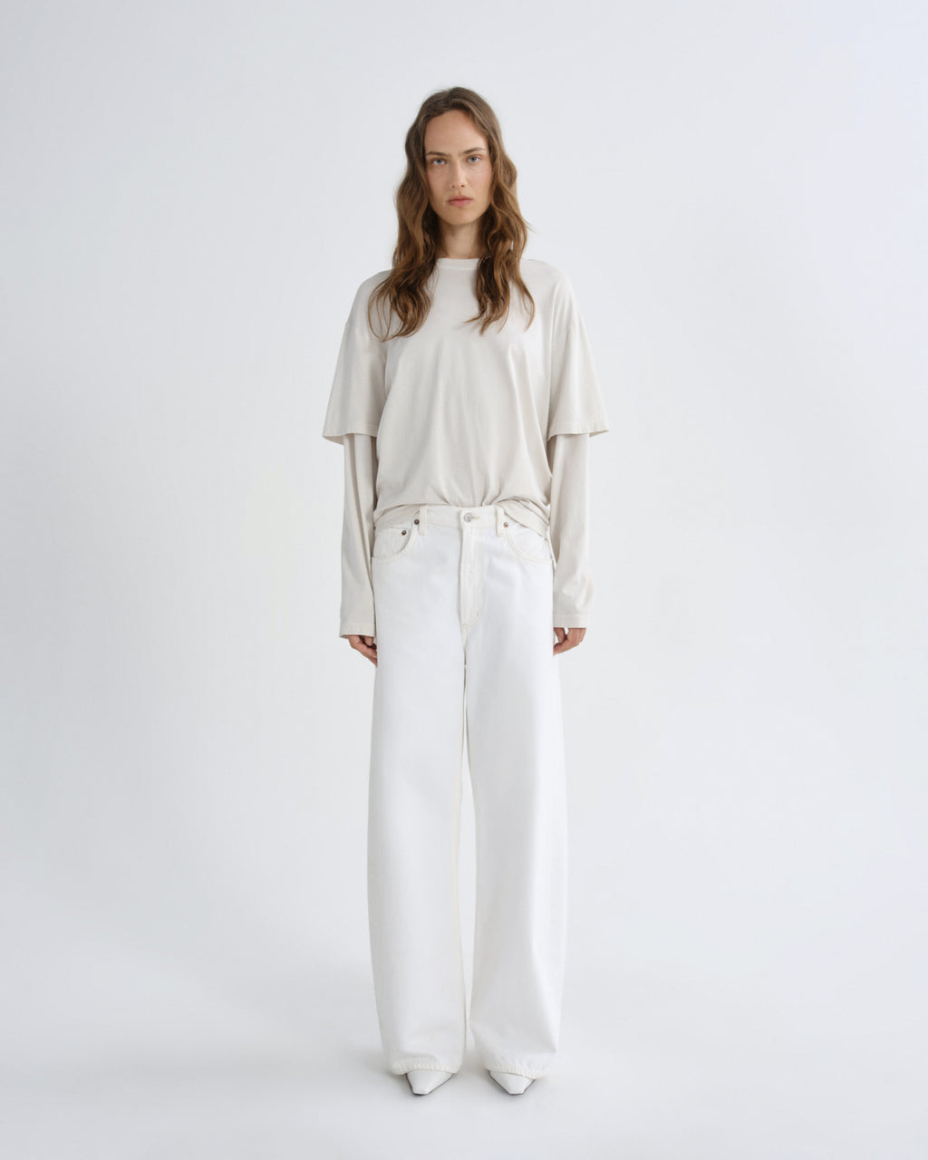 Woman wearing a beige top and white pants on a white background